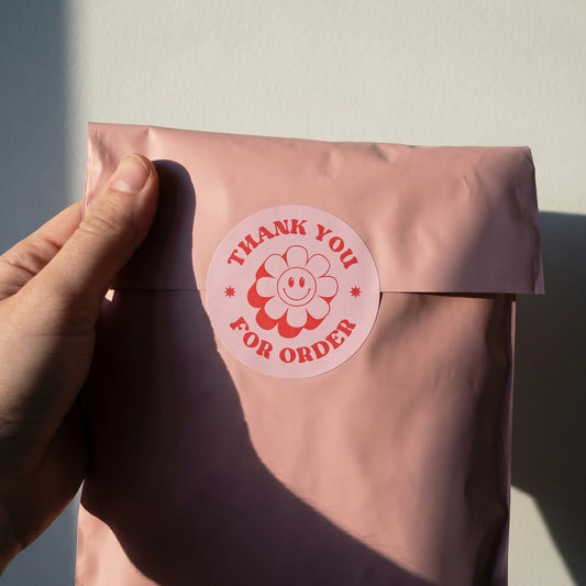 White tissue paper packaging tied with black ribbon, sealed with a Thank You Retro Groovy Daisy Varikit sticker reading 'Thank You'.