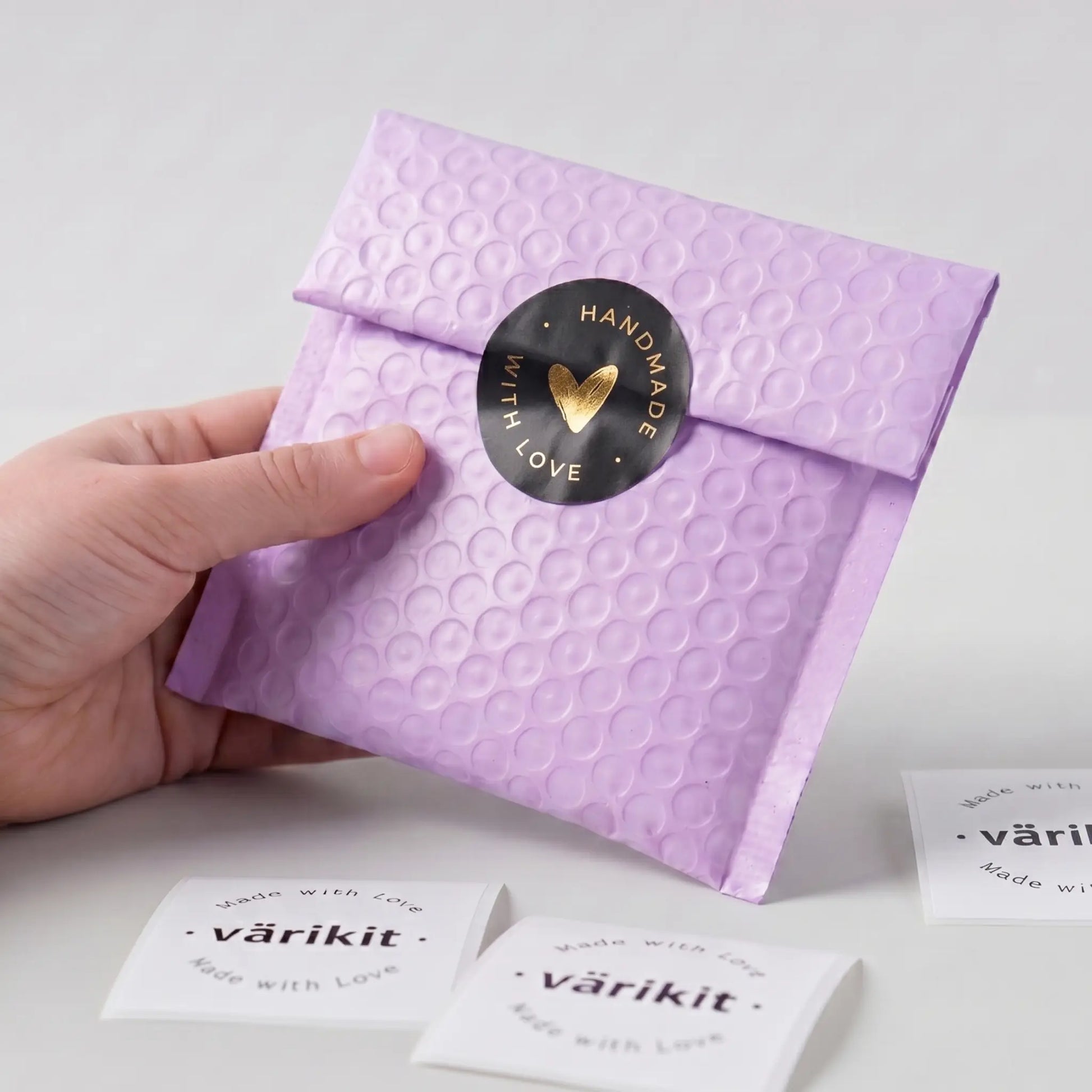 Hand holding a purple textured envelope with a 'Handmade with Love' sticker on a light gray background.