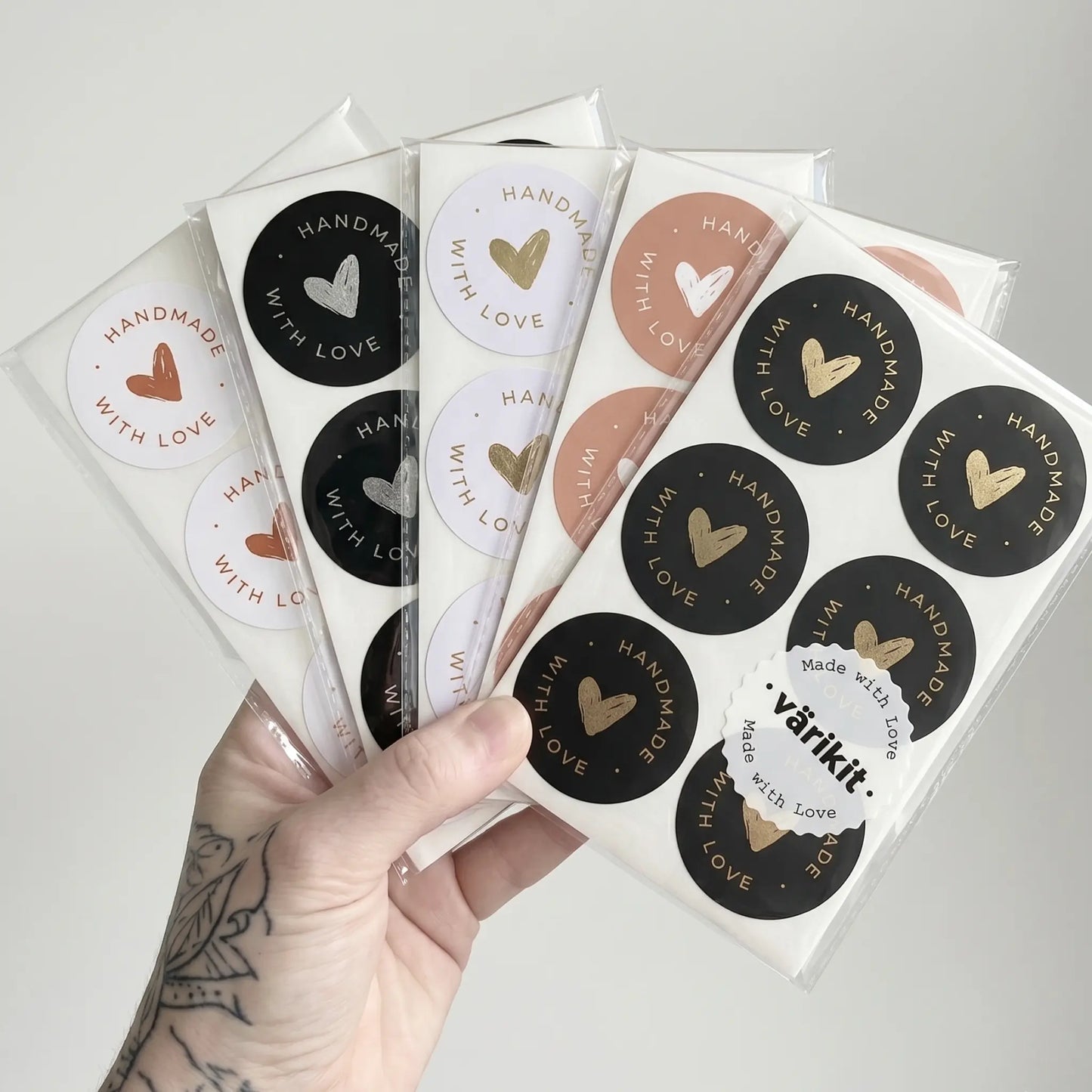 Hand holding a set of round stickers with 'Handmade with Love' text and heart designs.