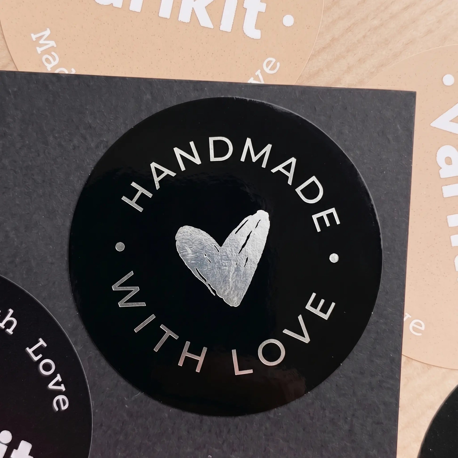 Black circular sticker with 'Handmade with Love' text and heart symbol on a cardboard background.