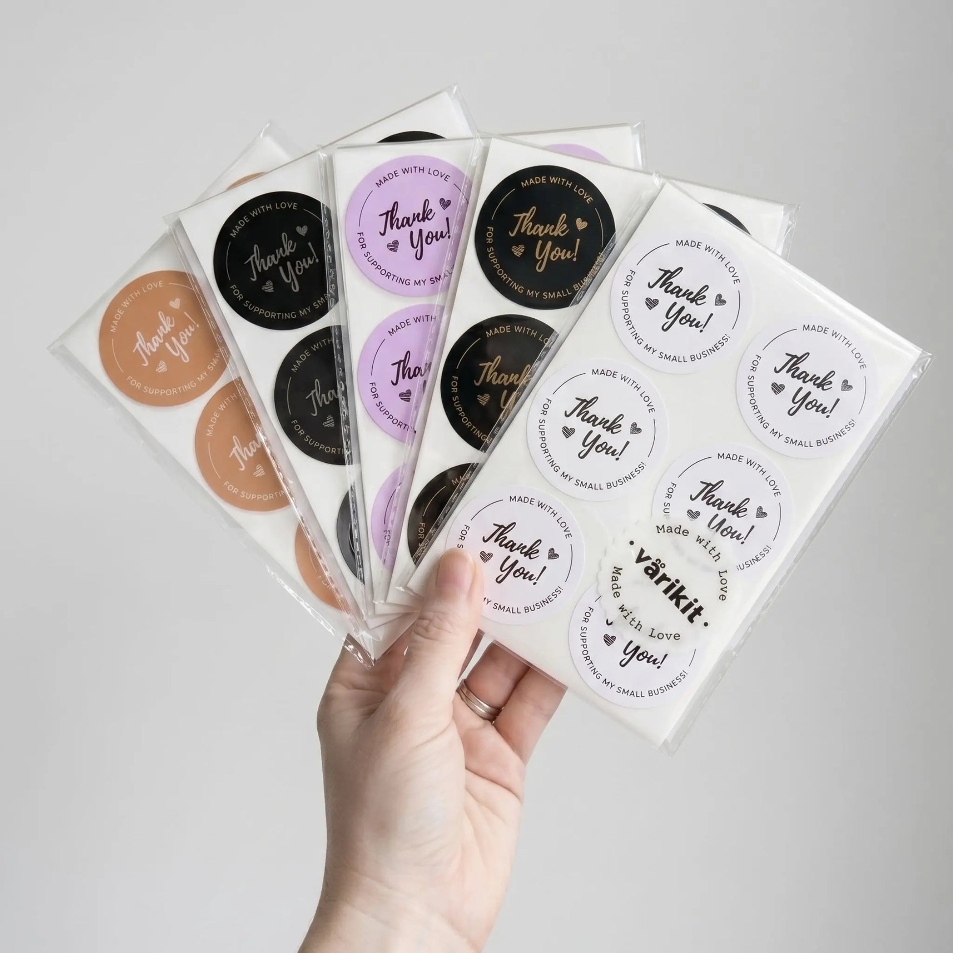 Hand holding several sheets of round stickers with 'Thank You' text on a light gray background