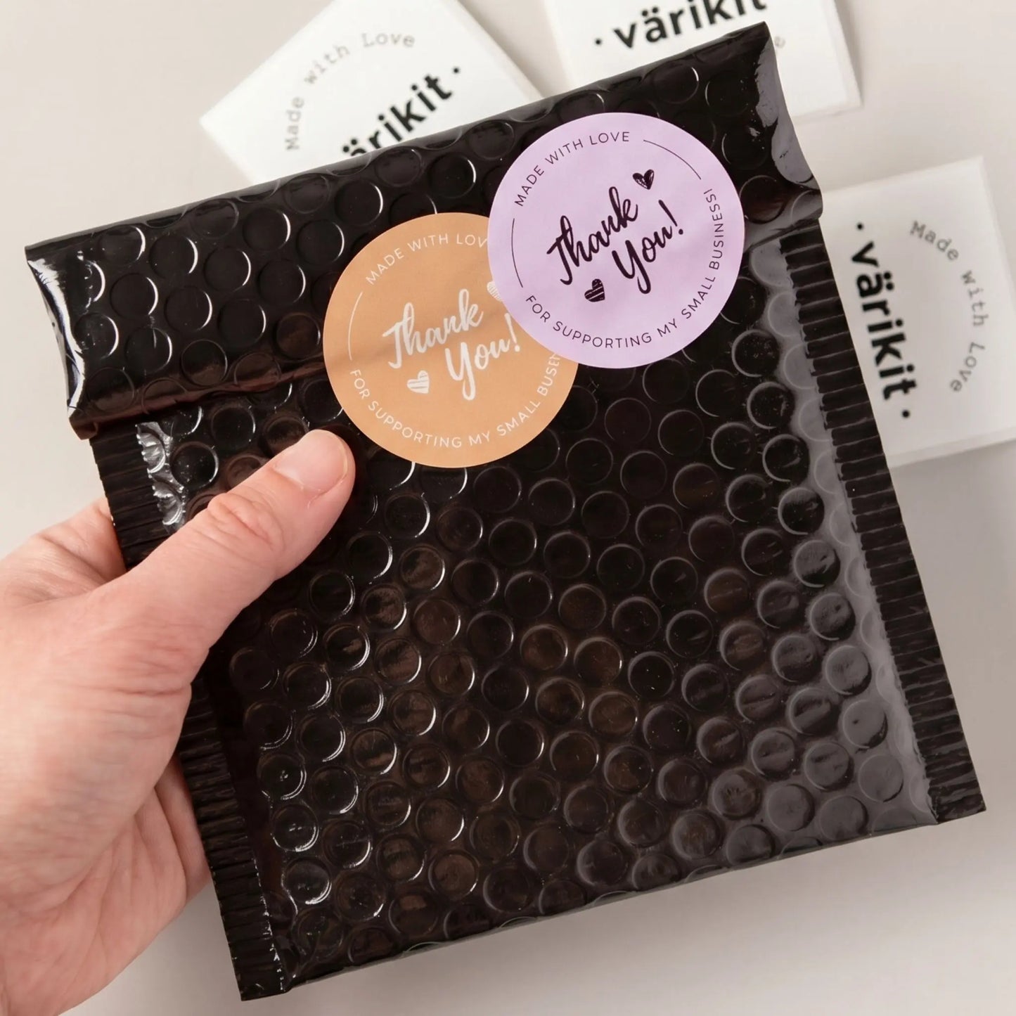 Bubble wrap package with 'Thank You!' stickers held by a hand, on a light background.