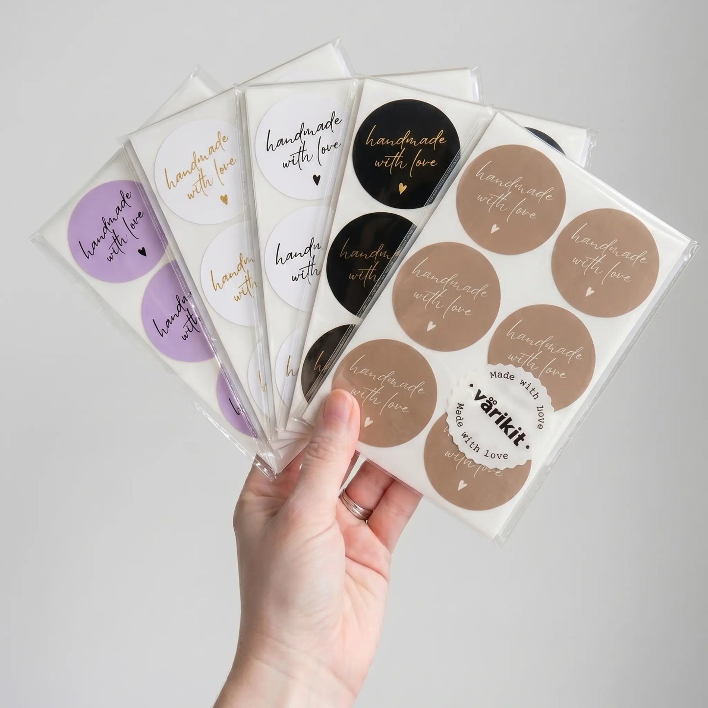 Handful of round stickers with 'handmade with love' text held by a hand on a light gray background