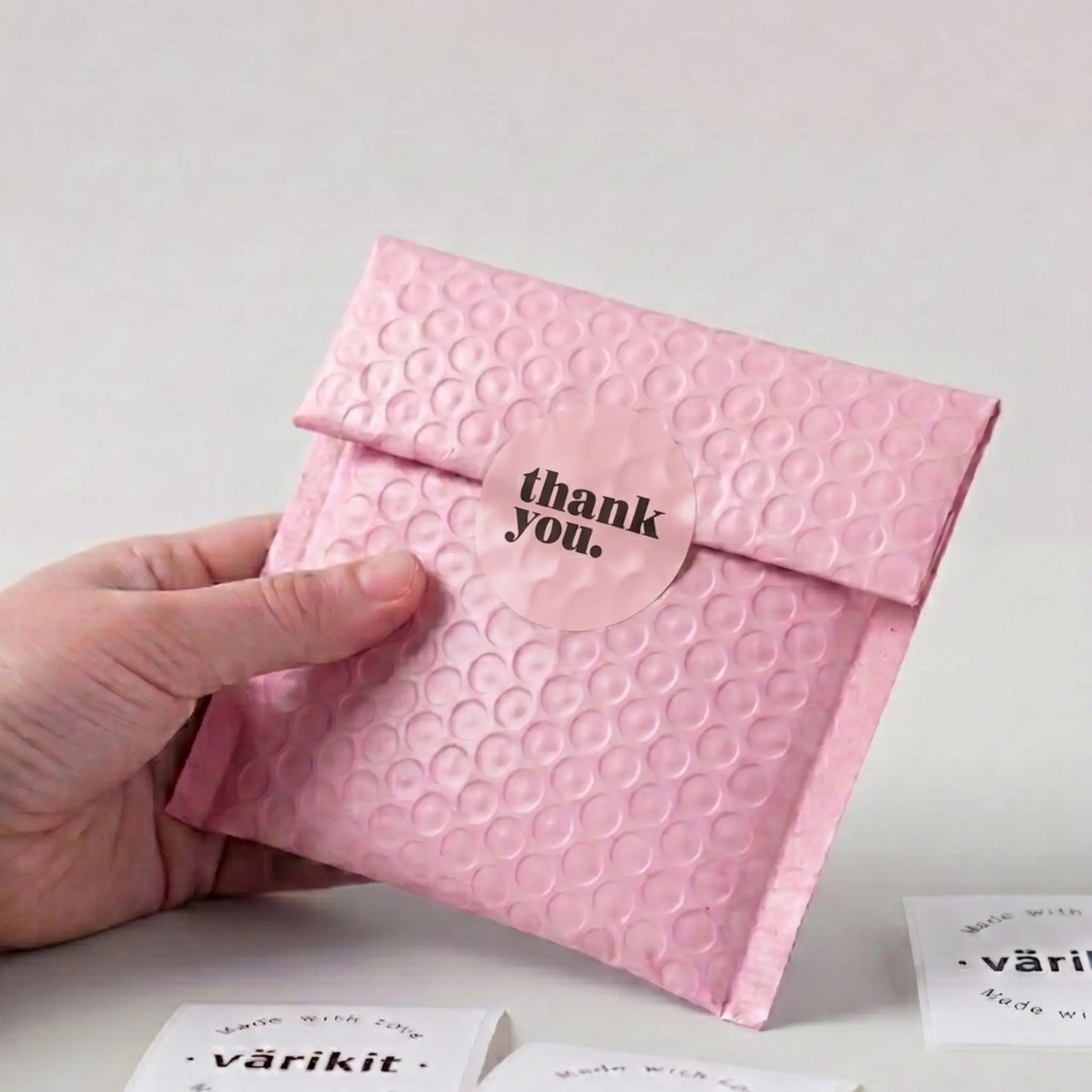 Pink textured envelope with 'thank you' sticker held by a hand on a light background