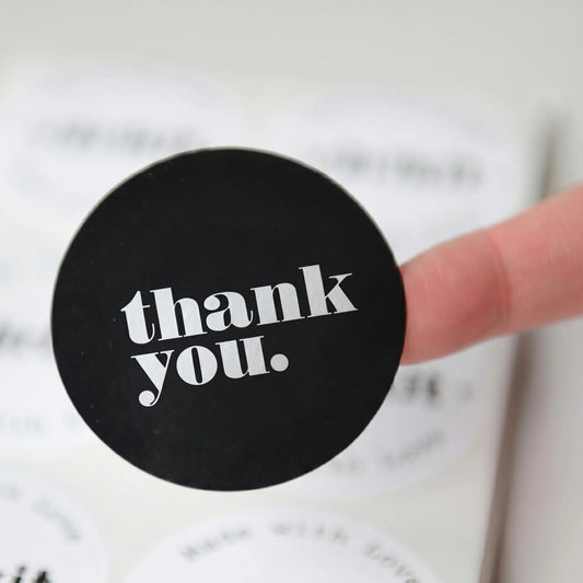Black circular coaster with 'thank you.' text held by a finger