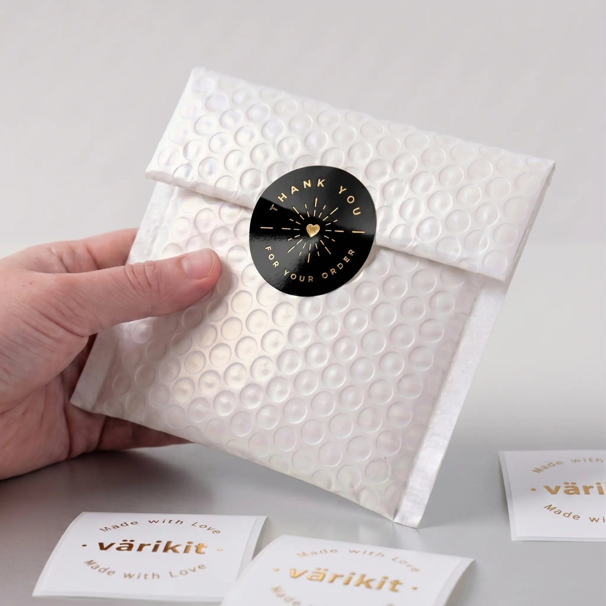 White textured package with a black gold foil circular label held by a hand on a light gray background