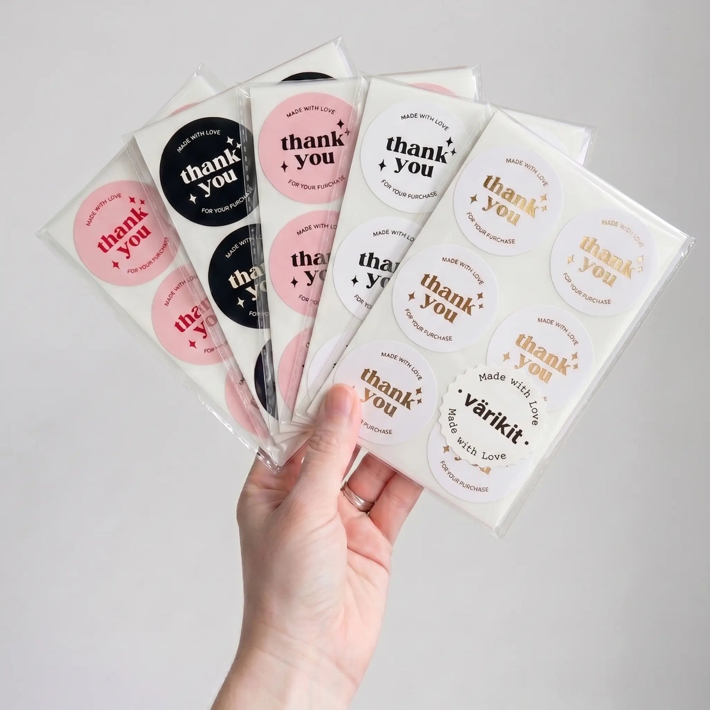 Hand holding packages of 'thank you' stickers with various designs.