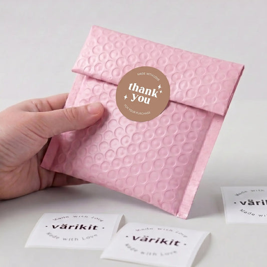 Pink textured envelope with a 'thank you' sticker held by a hand, on a light gray background.