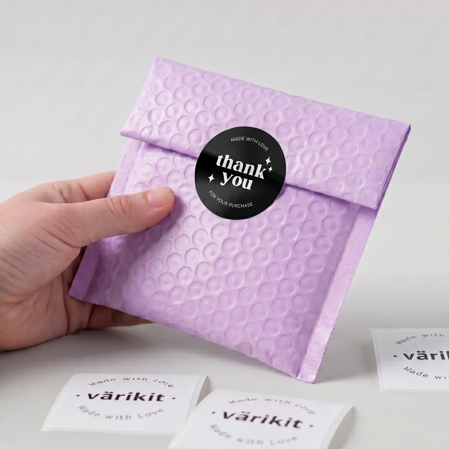 Hand holding a purple textured envelope with a 'thank you' sticker on a light gray background