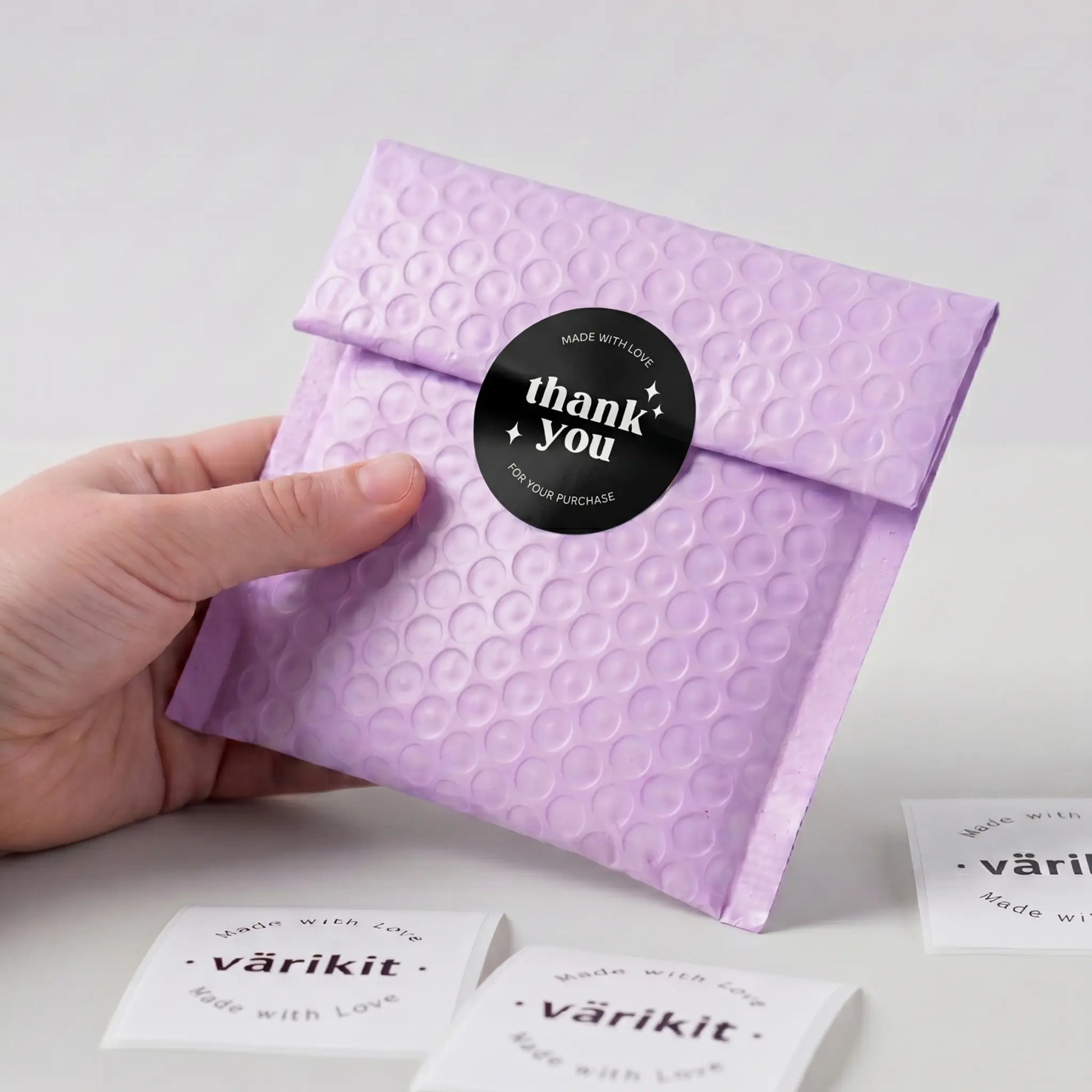 Hand holding a purple textured envelope with a 'thank you' sticker on a light gray background