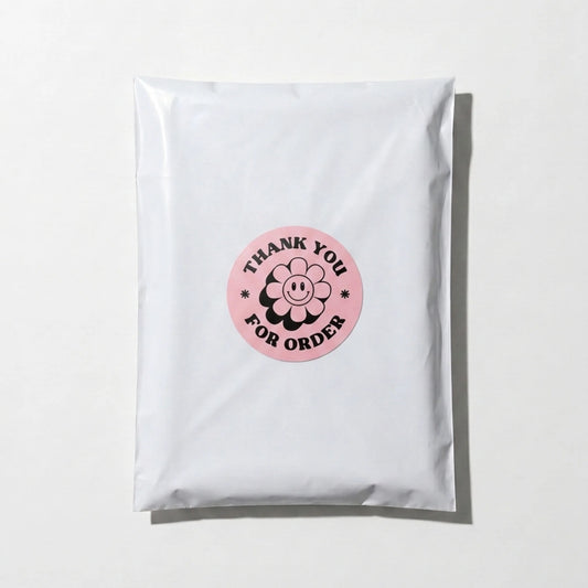 Pink 2-inch round Thank You sticker with black retro groovy daisy design, applied on a white poly mailer bag for small business packaging by Varikit