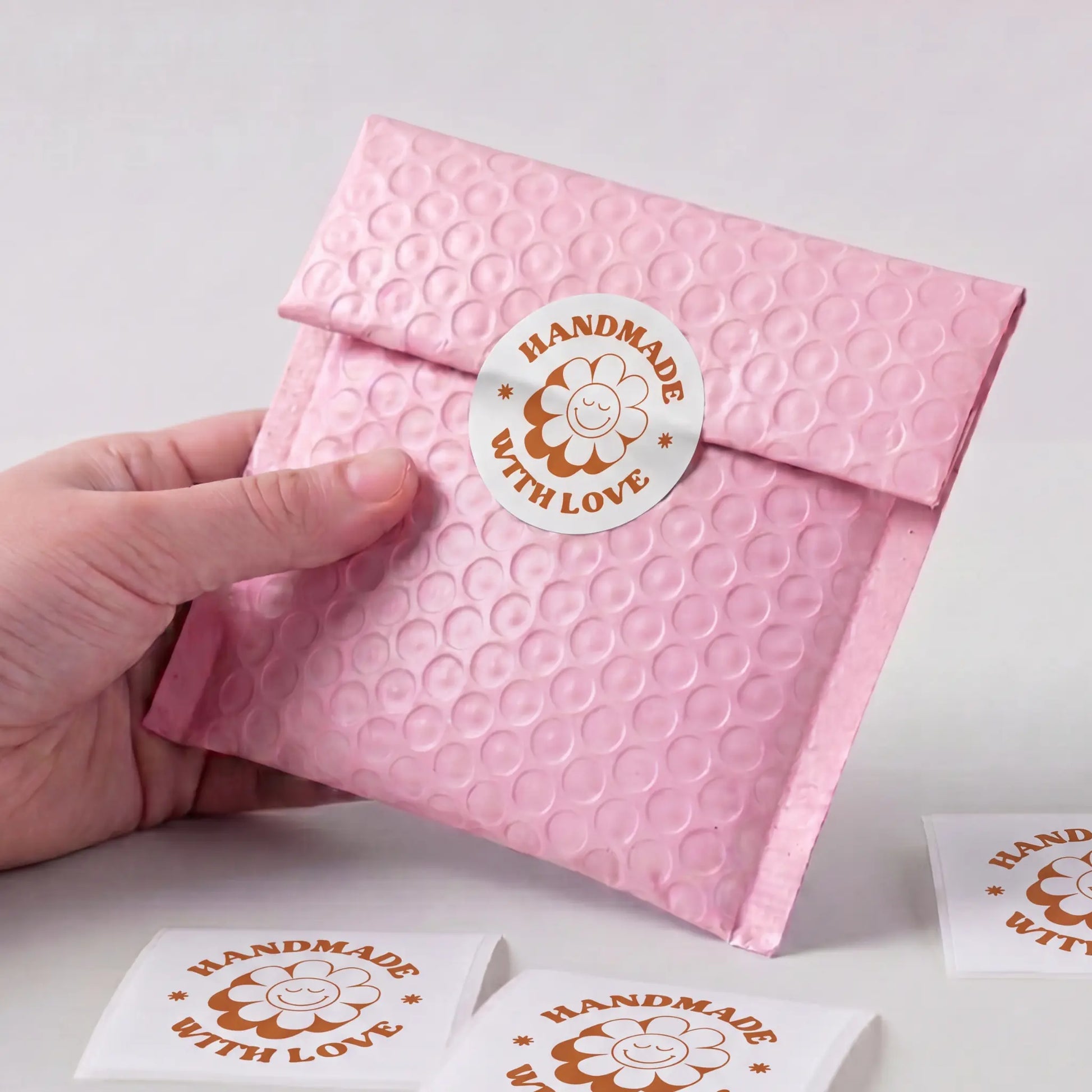 Pink textured envelope with a 'Handmade with Love' sticker held by a hand on a light background.