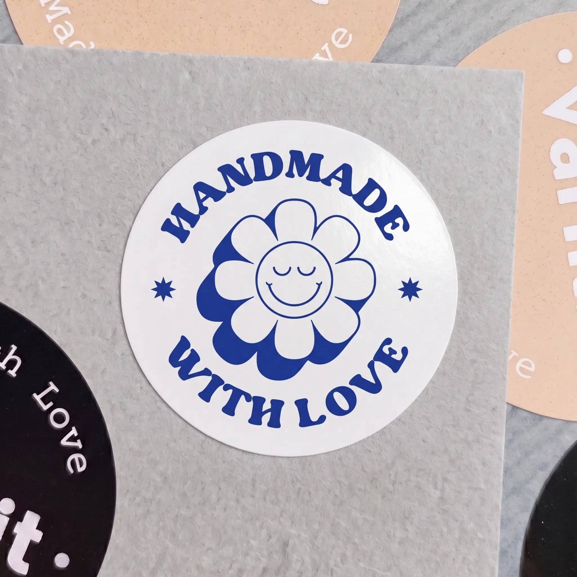 Round sticker with 'Handmade with Love' text and a flower design on a gray background.