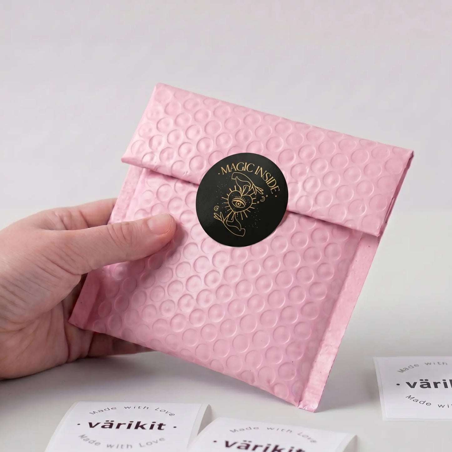 Hand holding a pink textured envelope with a black label on a light gray background