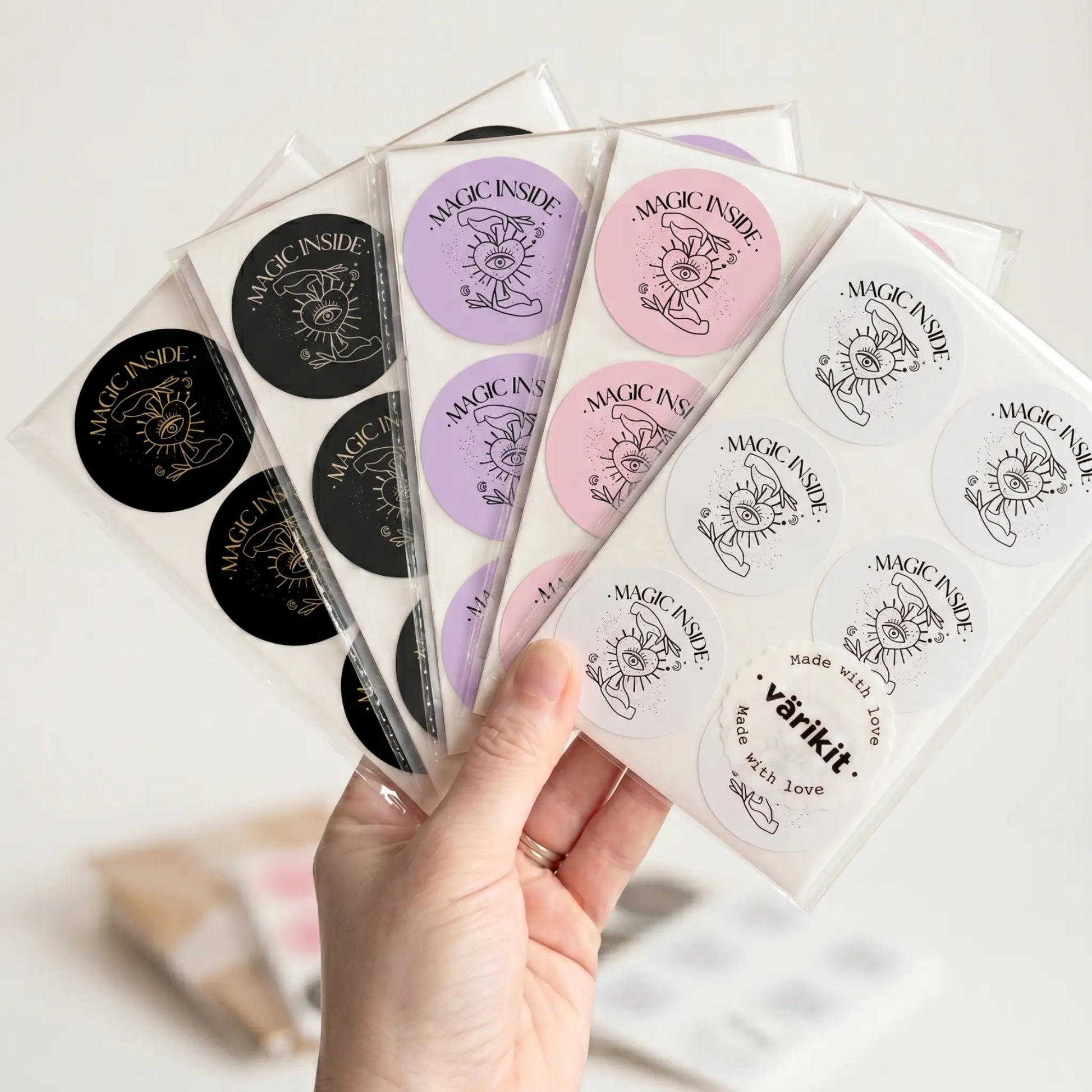 Hand holding packs of 'Magic Inside' stickers with various designs and colors.