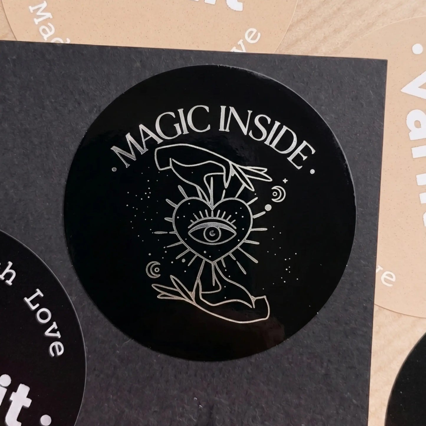 Black circular sticker with 'Magic Inside' text and mystical design on a textured surface.