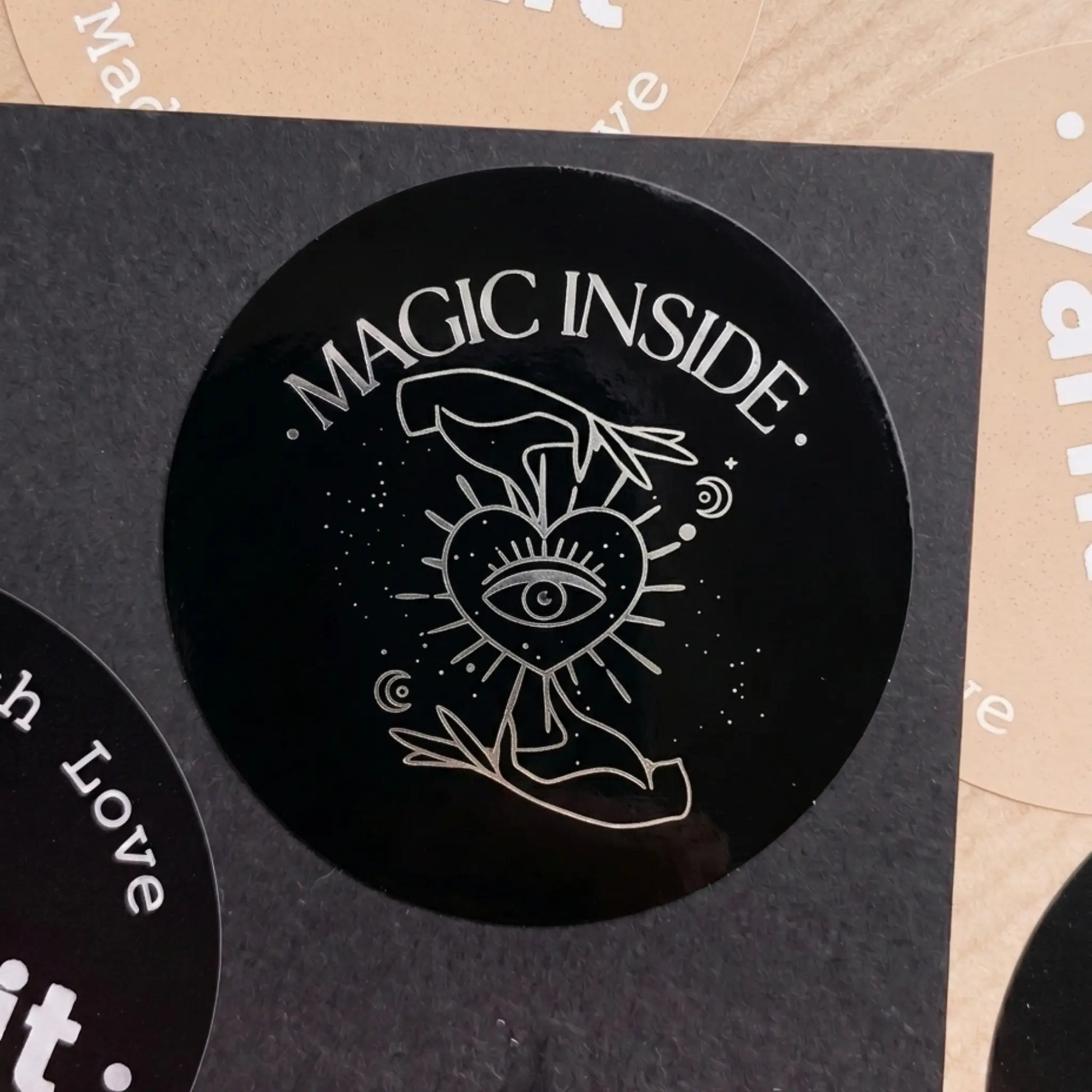 Black circular sticker with 'Magic Inside' text and mystical design on a textured surface.