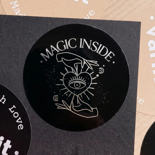 Black circular sticker with 'Magic Inside' text and mystical design on a textured surface.
