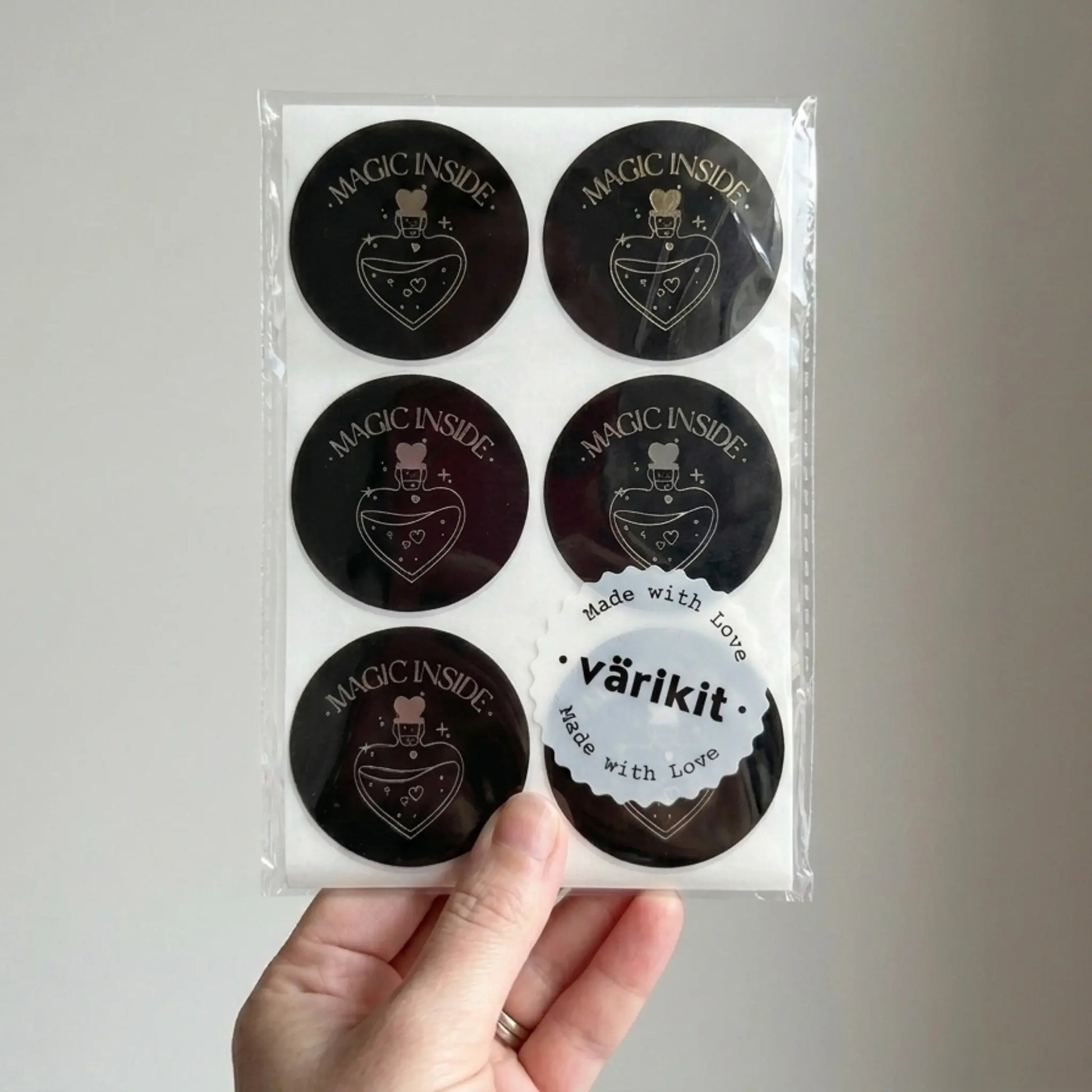 Pack of black circular stickers with 'Magic Inside' text held by a hand against a gray background