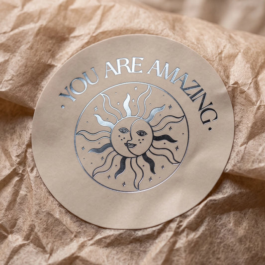White corrugated mailer box sealed with a Thank You Smiling Sun Moon Varikit sticker reading 'YOU ARE AMAZING'.