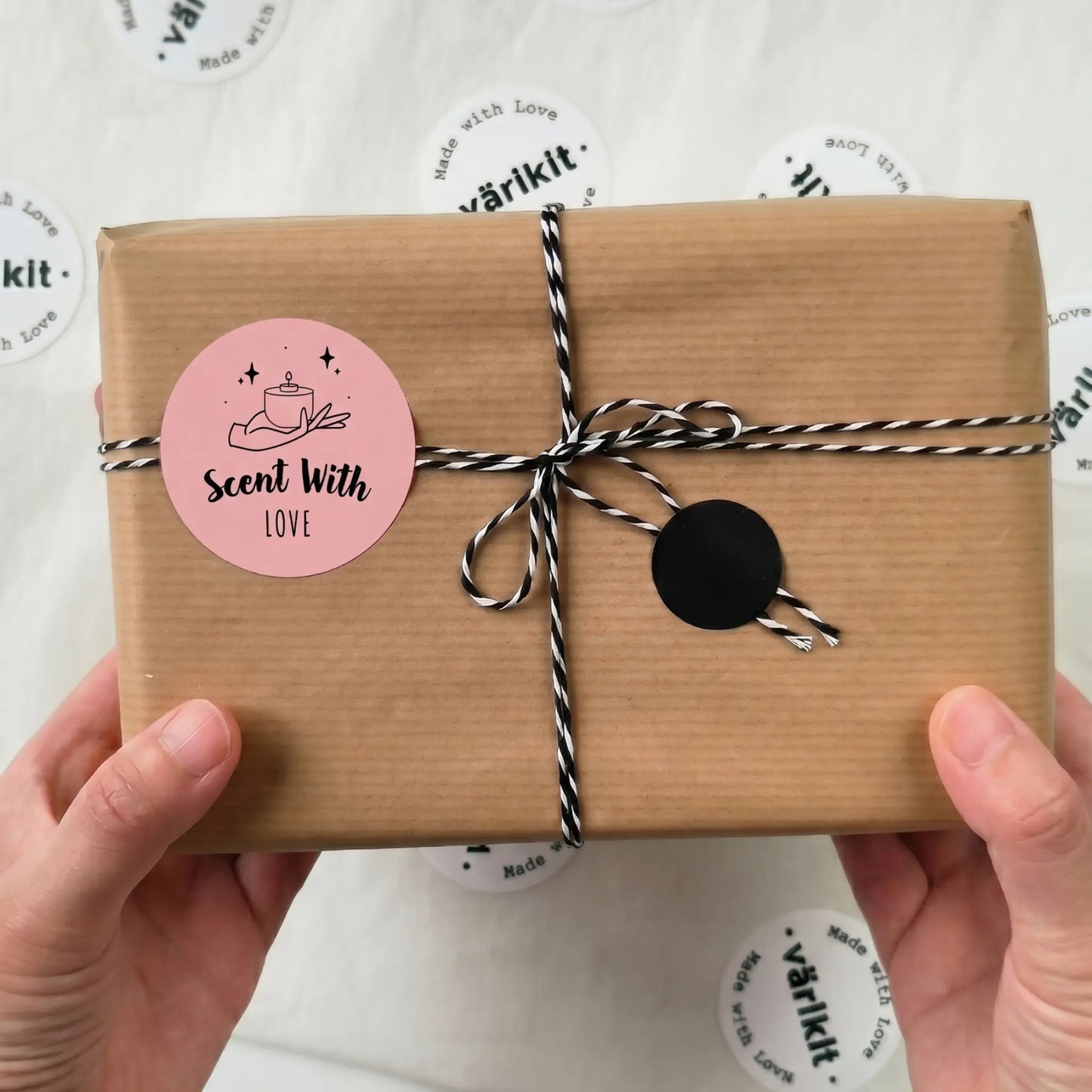 Gift box with brown paper wrap, pink 'Scent With Love' label, and black tie held by hands on a white background with 'varikit' branding.