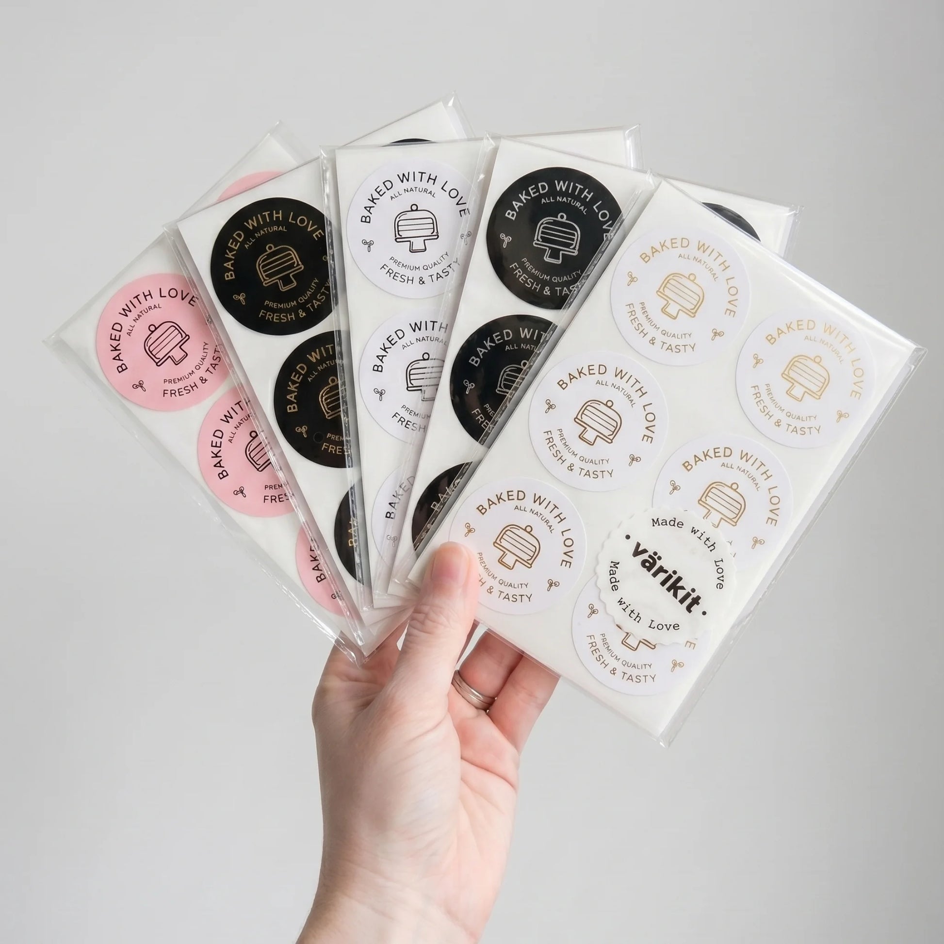 Hand holding multiple packages of 'varikit' baked goods ''baked with love' labels with visible branding.