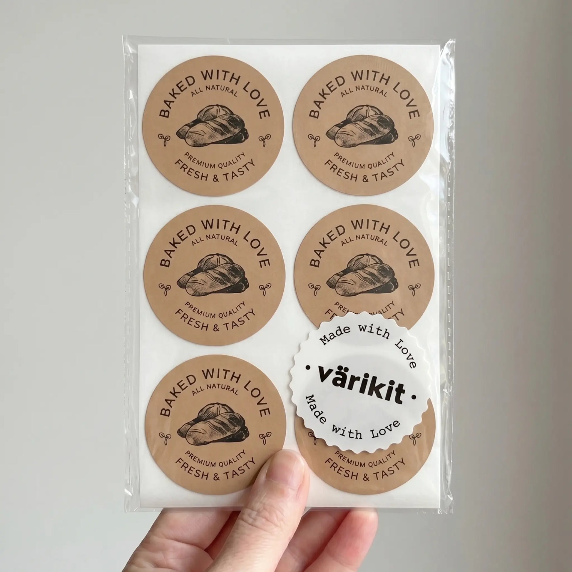 Packaging of 'Baked with Love' stickers held by a hand on a light gray background