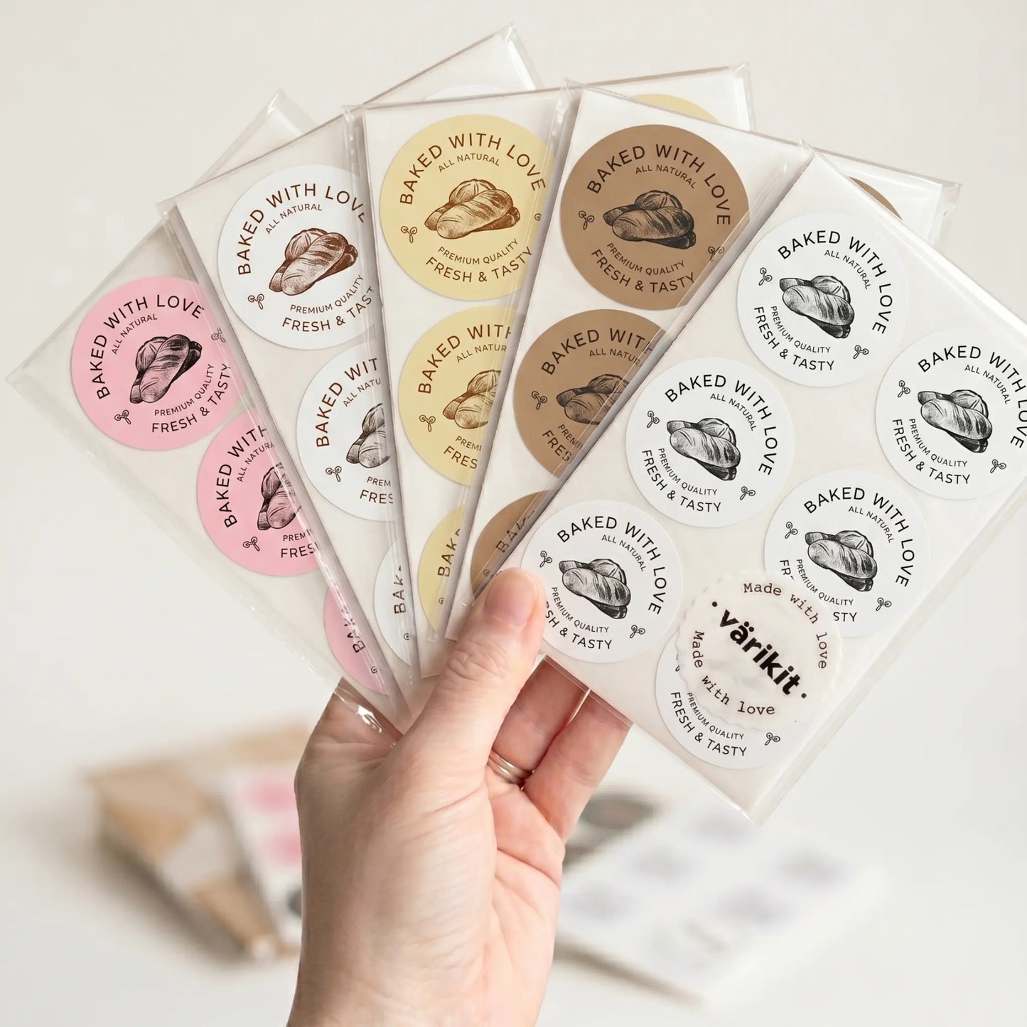 Hand holding a set of 'Baked with Love' stickers with various color schemes.