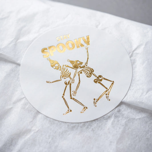 White corrugated cardboard box sealed with a Playful Stay Spooky Dancing Skeletons Varikit sticker reading 'STAY SPOOKY'.