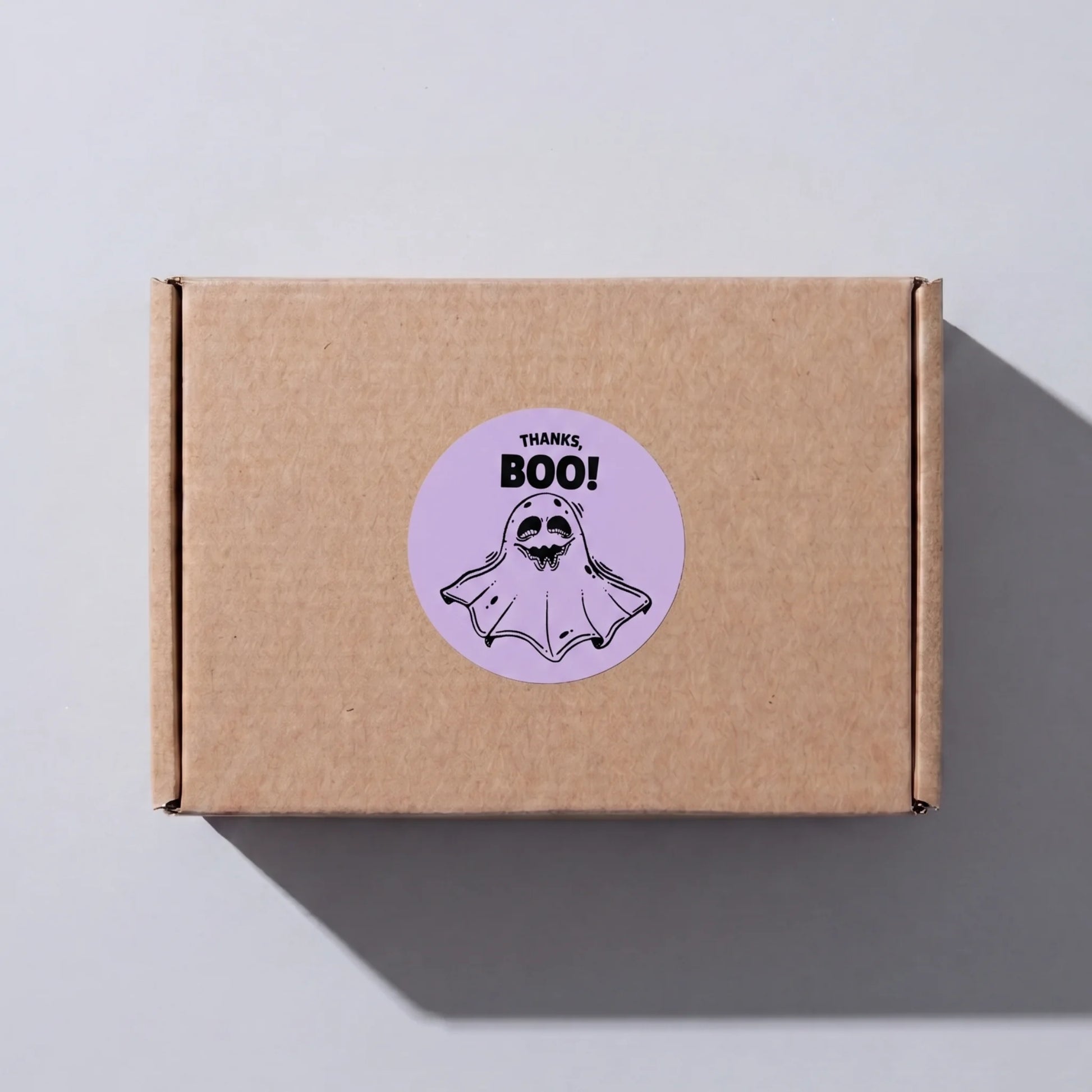 Brown kraft corrugated mailer box sealed with a Playful Thank You Thanks Boo Ghost Varikit sticker reading 'THANKS, BOO!'.