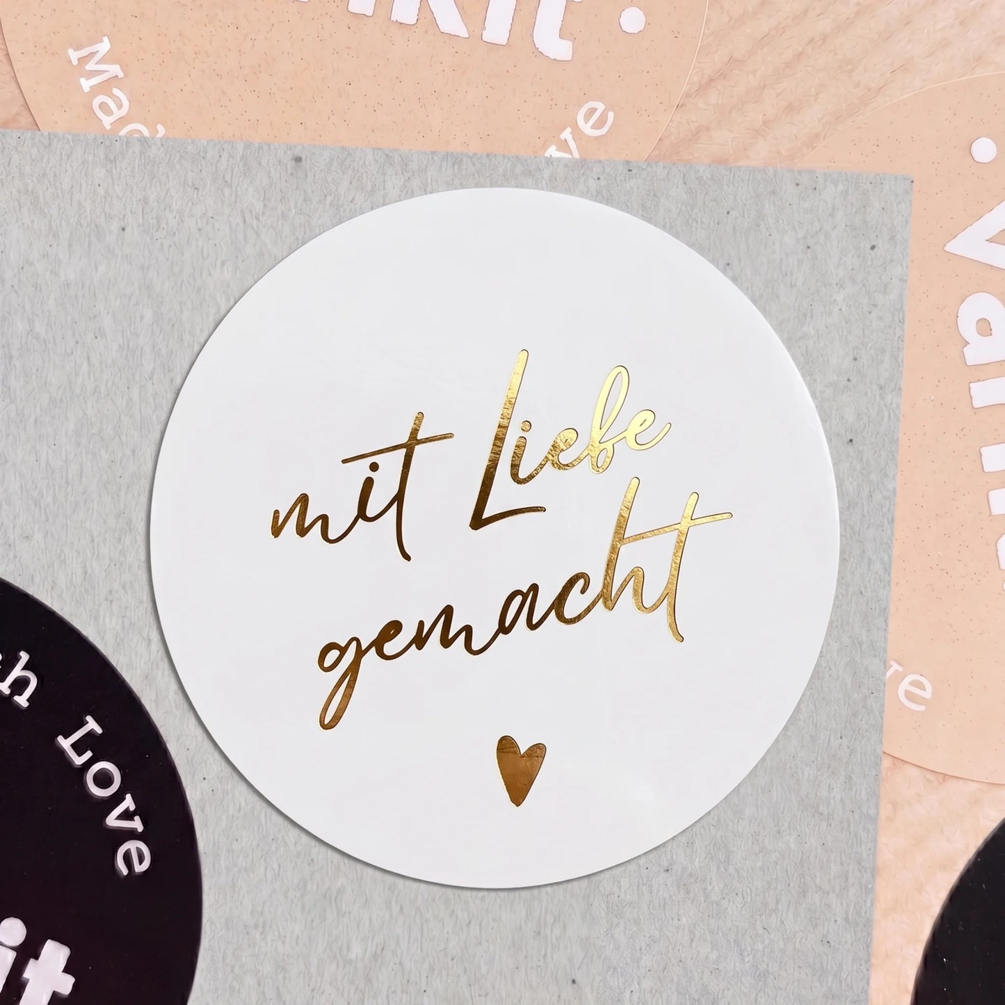 Round white sticker with gold text 'mit Liebe gemacht' on a gray background